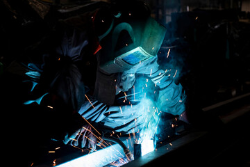 An experienced worker in a dark workshop welds metal for billets.