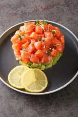 Raw salmon, avocado salad tartare served in culinary ring on black plate. Grey concrete background