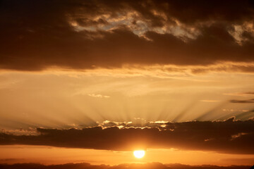 Background of a warm sun between clouds with sunbeams at sunset