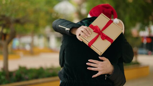 Mother and son wearing christmas hat surprise with gift at park