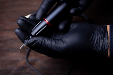 the hands of a permanent makeup artist in black sterile gloves shows a close-up of a tattoo machine on which a tattoo cartridge is worn