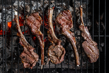 Grilled lamb mutton chop steaks on barbecue, outdoor BBQ grill with fire. Top view