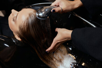 Hairdresser in beauty salon washes his client hair, before procedure of applying natural restoring...