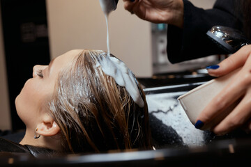 Hairdresser in beauty salon washes his client hair, before procedure of applying natural restoring ingredients and vitamins to hair and haircut.
