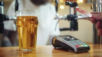 Buying beer and paying by credit bank card via terminal close-up. Bearded barman standing behind bar counter. Contactless payment in restaurant, touch-free shopping in pubs.