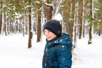 Defocus smiling child boy in winter forest in snowstorm with snowball on head. Funny kid  on snowy...