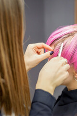 Fototapeta premium Hairdresser prepares dyed short pink hair of a young woman to procedures in a beauty salon