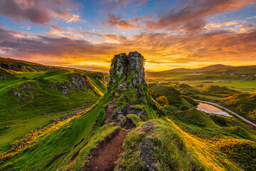 Sunset on the Isle of Skye in Scotland. Castle Ewen mountain hill with paths and meadow in the evening. Red and orange clouds in the sky. small lake with road. Sunshine in the valley