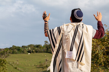 Horizontal photo of Juido Latino wearing tefilin and kippah raising his hands praying while looking...