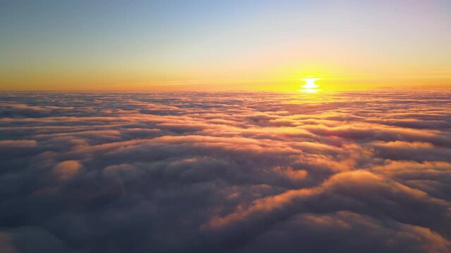 Aerial view from above at high altitude of dense puffy cumulus clouds flying in evening. Amazing sunset from airplane window point of view