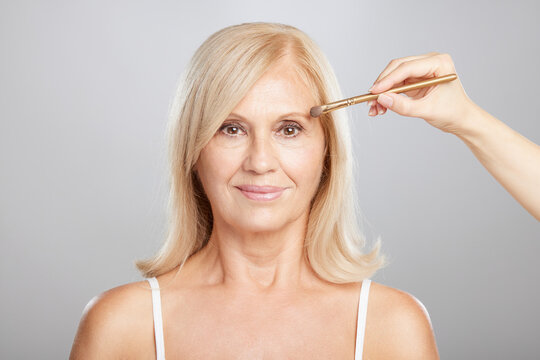 A Happy Senior Blond Woman Getting Her Make Over Done. A Beautician Putting Make-up On Senior Woman's Face