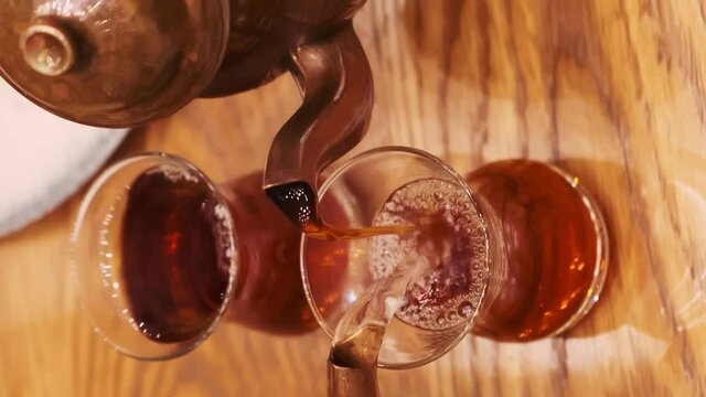 The girl pours Turkish aromatic tea into a traditional glass. Tea from two teapots is poured into a glass. Tea is poured from one teapot. Water is poured from another kettle. Close-up. Steam rises abo