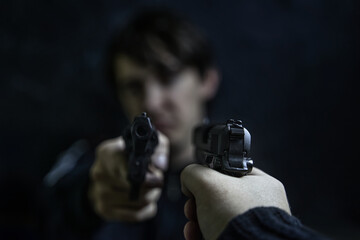 Two men point guns at each other. Threat to life. Close-up of hand with pistol. Shootout of criminals with revolvers. Dark background and dangerous situation. Killer or murderer.