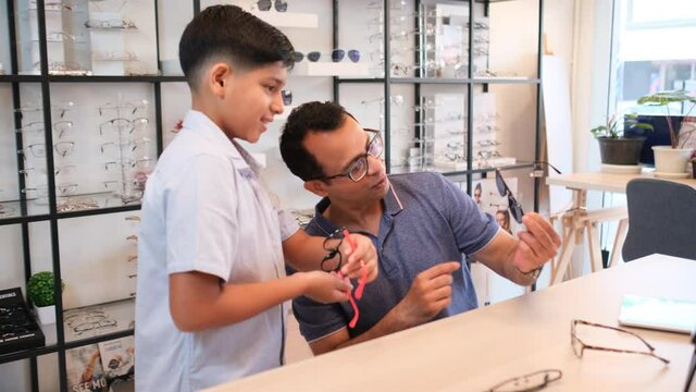 Indian father sit and discuss with his son to select eyeglasses or sunglasses in optical shop with happiness of good activity together.