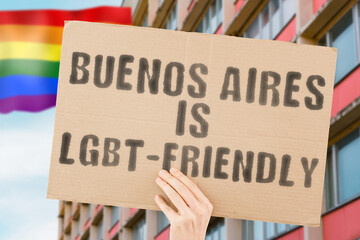 The phrase " Buenos Aires is LGBT-Friendly " on a banner in men's hand with blurred LGBT flag on the background. Human relationships. different. Diverse. liberty. Sexuality. Social issues. Society