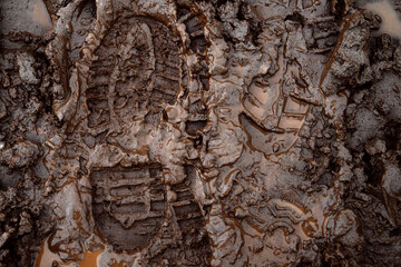 A boot print in the mud close-up. Footprint in the dirt. Bottom of shoes.