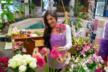Beautiful florist carefully choosing and smelling flowers for the bouquet she need to make