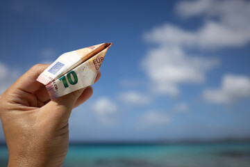 Hand holding the plane made of 10 euros bill on the background on seascape.