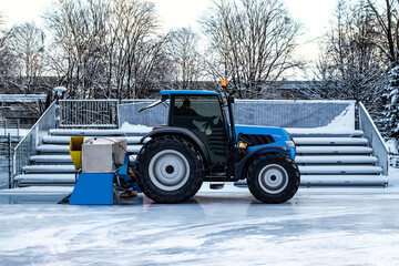 Side view of a new tractor and a resurfacer polishing an ice skating rink with a tribune in the background and copy space on ice surface