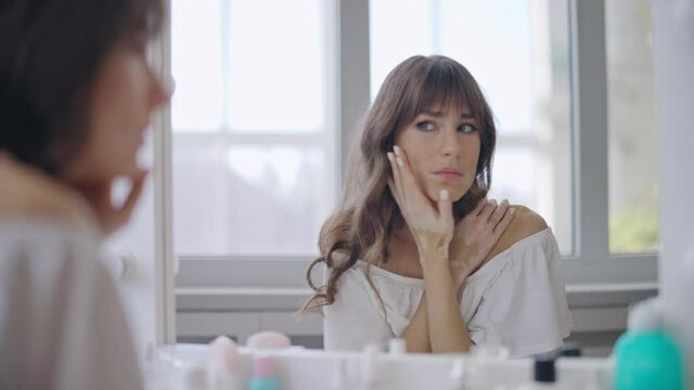 Sad young woman with vitiligo skin looking in mirror, appearance insecurities