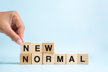 Woman hand arranging wooden cubes with NEW NORMAL word.