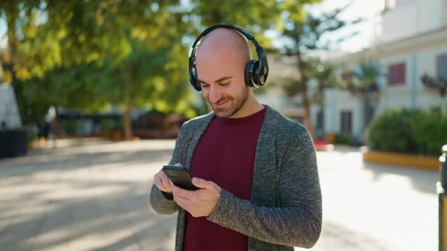 Young bald man smiling confident listening to music at park