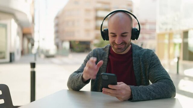 Young bald man smiling confident listening to music at coffee shop terrace