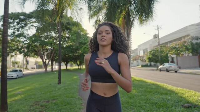 Latin woman runner running in central median of city street. Female jogger training for marathon as part of active healthy lifestyle. Slow motion young woman jogging. Cinematic 4K