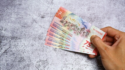 A man's hand is making a payment. Male hand showing Indonesian rupiah note. Indonesian Rupiah the...