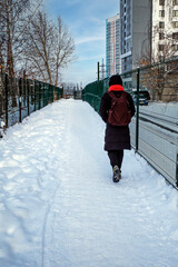 A man with a backpack walks along a snow-covered sidewalk on a winter day