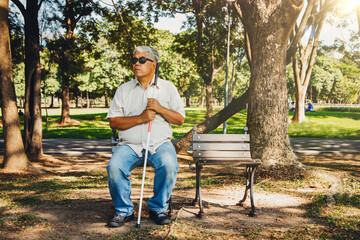 The joy of an aging asian old man with a walking stick sat alone in a wooden chair in the afternoon...