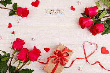 Red roses, a gift box made of craft paper with a red ribbon, the inscription love on a white wooden background. Valentine's Day, Mother's Day, Birthday. Top view, copy space.
