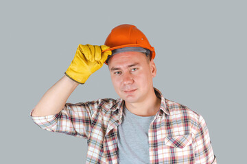 Portrait of a working man in an orange helmet and gloves, a worker holding a helmet with his hand...