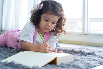 Cute little girl lying on the floor and drawing on book