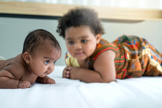Dark skinned girl lying on bed and looking at younger sister, sibling relationship concept