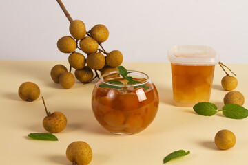 Longan drink in glass with fresh fruit peel the skin show white meat and black seed on a color background.