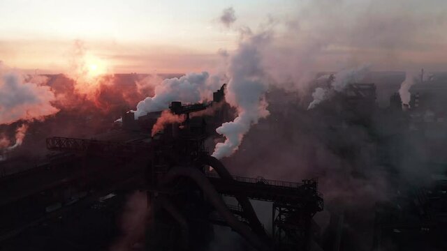 Drone around toxic enterprise chimneys tubing against the sky background release smoke. Factory pollutes environment. Aerial view