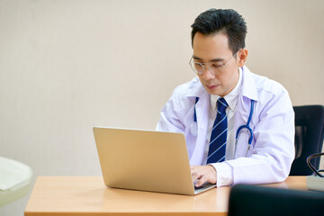 Asian male doctor use laptop find case of patient in hospital office room