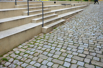 concrete staircase serves as a theater bench overlooking river. cobblestone cobblestones cubes on promenade with wooden benches. you can also sit on long wide stairs lined with tropical wood. drain 