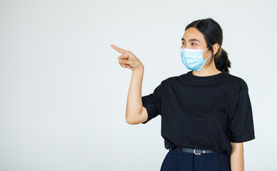 Portrait Asian woman wearing a face mask poses, pointing advertisement on white background, blank copy space with isolated white background cutout.