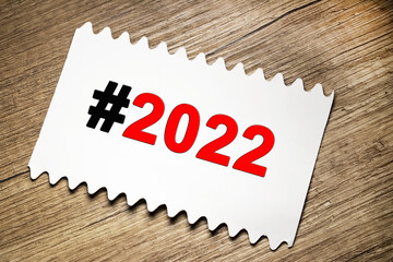 A hashtag with the number 2022 is written on a white sheet. New Year. Wooden table