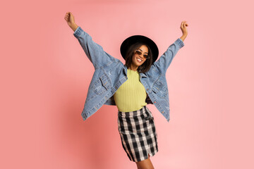 Ecstatic laughing  african woman in black hat and jeans jacket having fun  on pink background in...