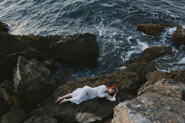 Barefoot woman in a white dress lying on a stone in a white dress view from above