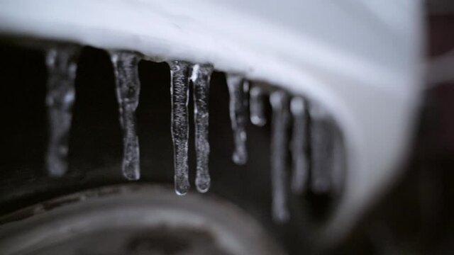 Ice icicles hanging on the fender of a white car close-up