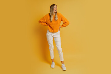 Fototapeta na wymiar Blond woman with suprice face in orange stylish autumn sweater posing over yellow background in studio. Full lenght.