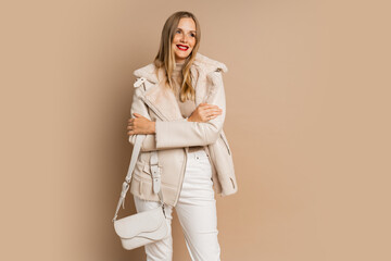 Pretty legant blond woman with red lips wearing trendy eco leather jacket , posing over beige background.  Winter fashion trends.