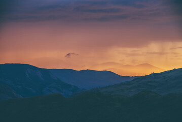 Atmospheric landscape with silhouettes of mountains with trees on background of vivid orange blue lilac dawn sky. Colorful nature scenery with sunset or sunrise of illuminating color. Sundown paysage.