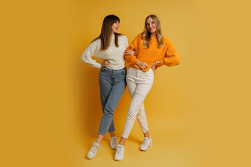 Two pretty women , best friends in stylish autumn  casual clothes having fun  over yellow...