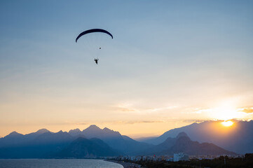 Silhouette of a man on a paraglider flying over the sea at sunset.