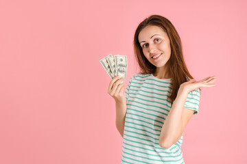 A freelancer girl in casual clothes smiles and holds hundred dollar bills in her hands standing on a pink background